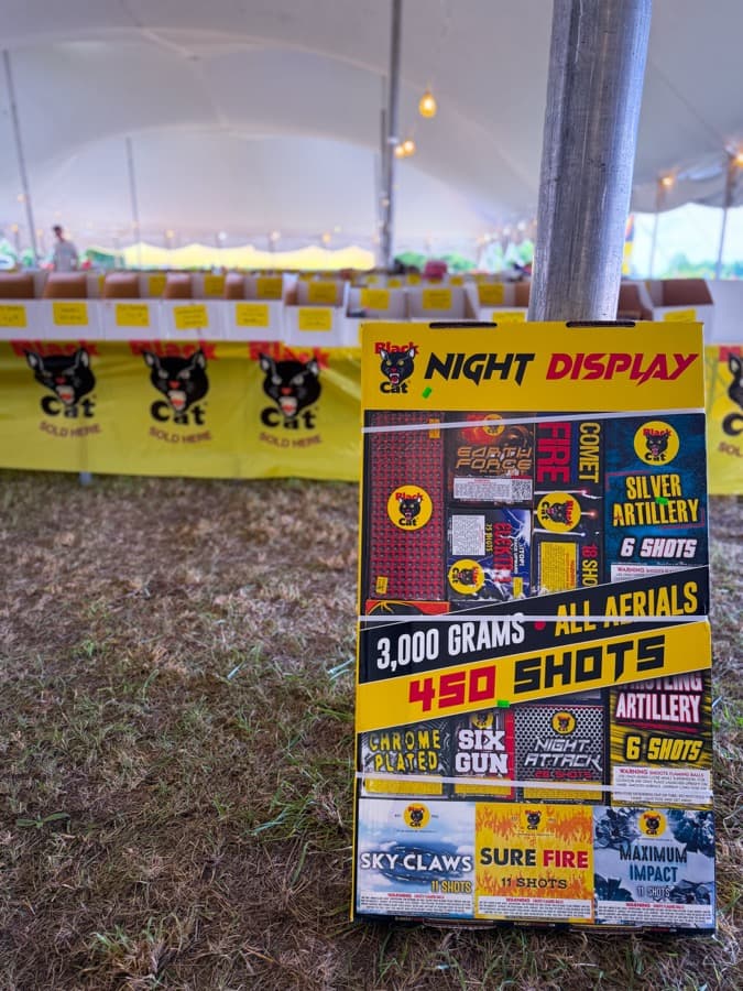 Crazy Joe's "Night Display" 3,000-gram, 450-shot fireworks assortment box on display in front of yellow Black Cat tablecloths under the tent